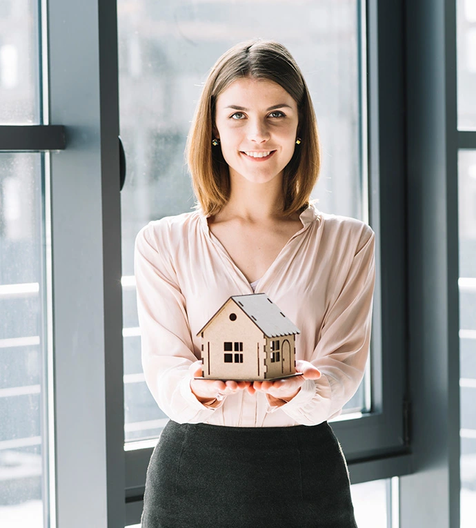 A smiling woman holding out a miniature model of a house