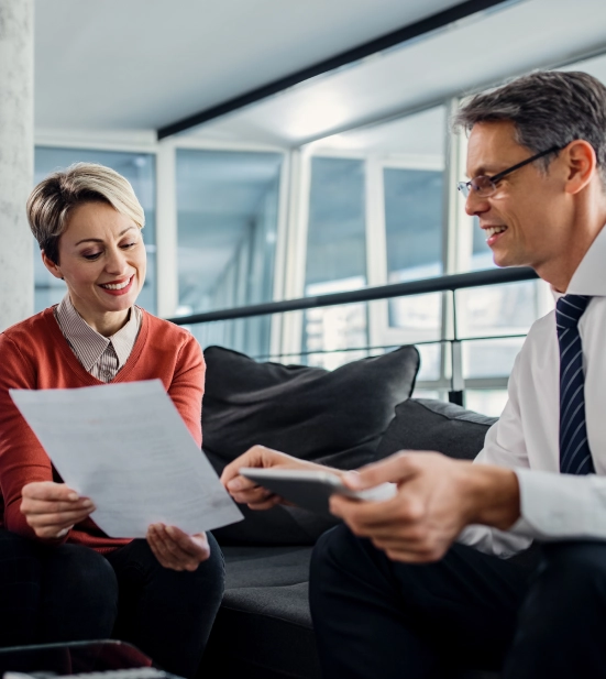 Alt A businessman and woman sitting on a couch, reviewing paperwork together.