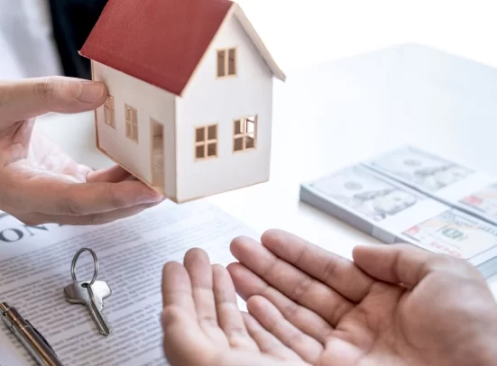 Alt A man holding a house model over a desk with keys