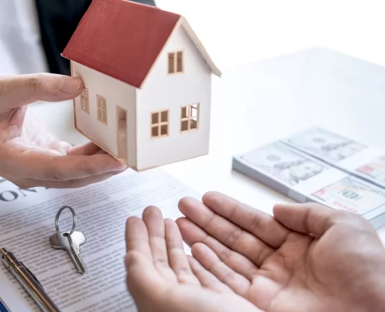 Alt A man holding a house model over a desk with keys