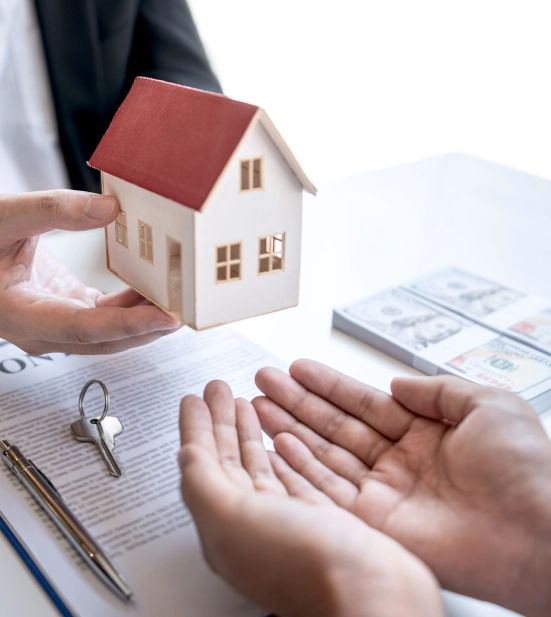 Alt A man holding a house model over a desk with keys