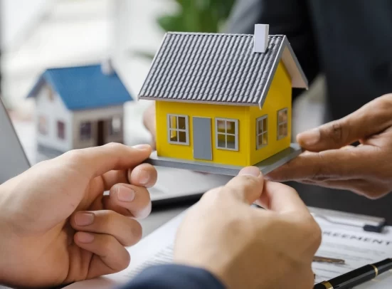 Alt A person passing a yellow miniature model of a house to another person