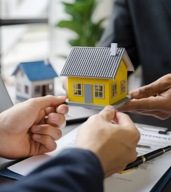 Alt A person passing a yellow miniature model of a house to another person