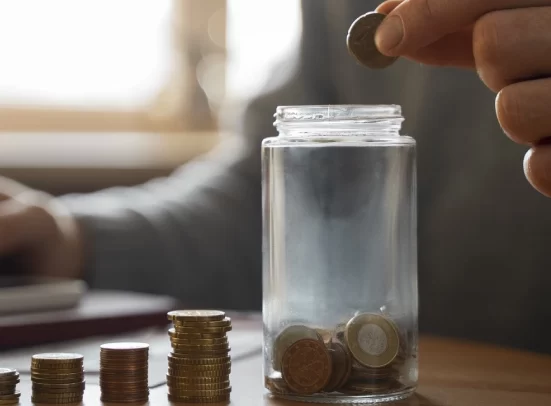 A person storing coins in a glass bottle