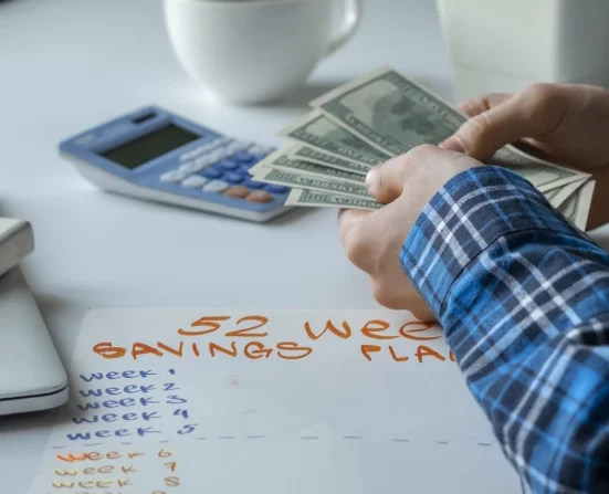 Alt A person counting dollar bills and planning a 52 week savings plan