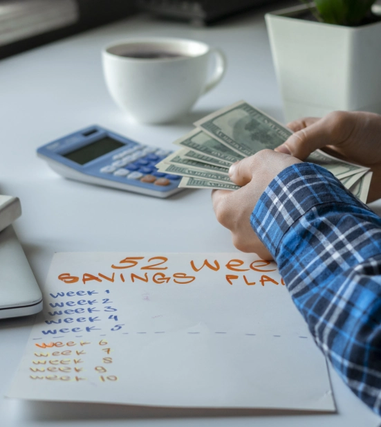 Alt A person counting dollar bills and planning a 52 week savings plan