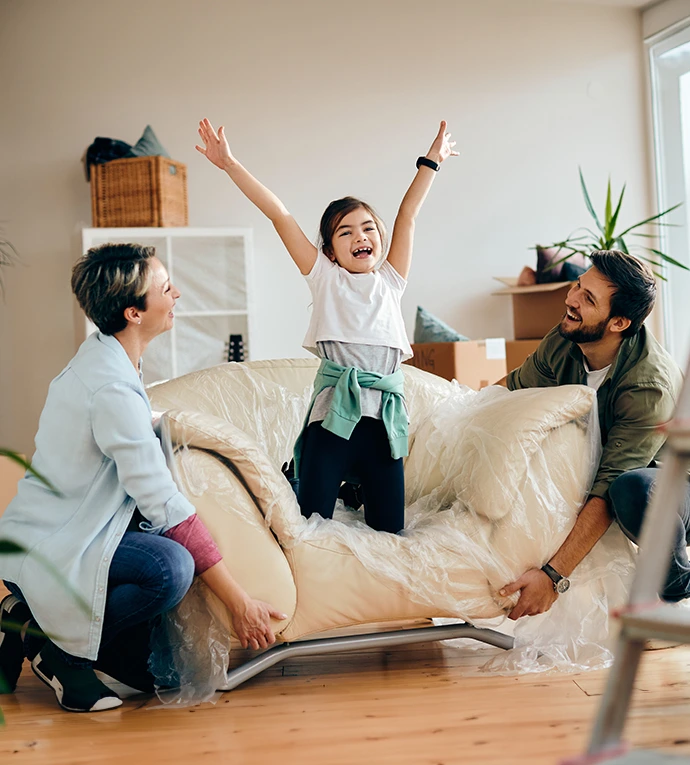 A child with raised hand on a chair surrounded by her parents