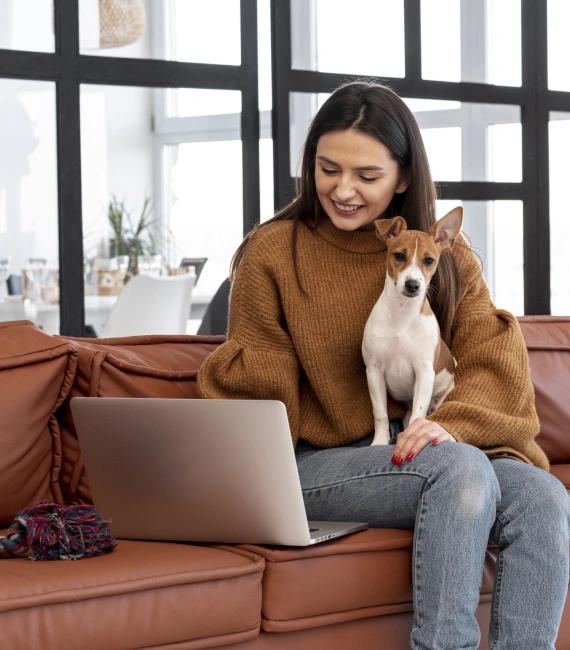 A happy woman holding a dog looking at a laptop